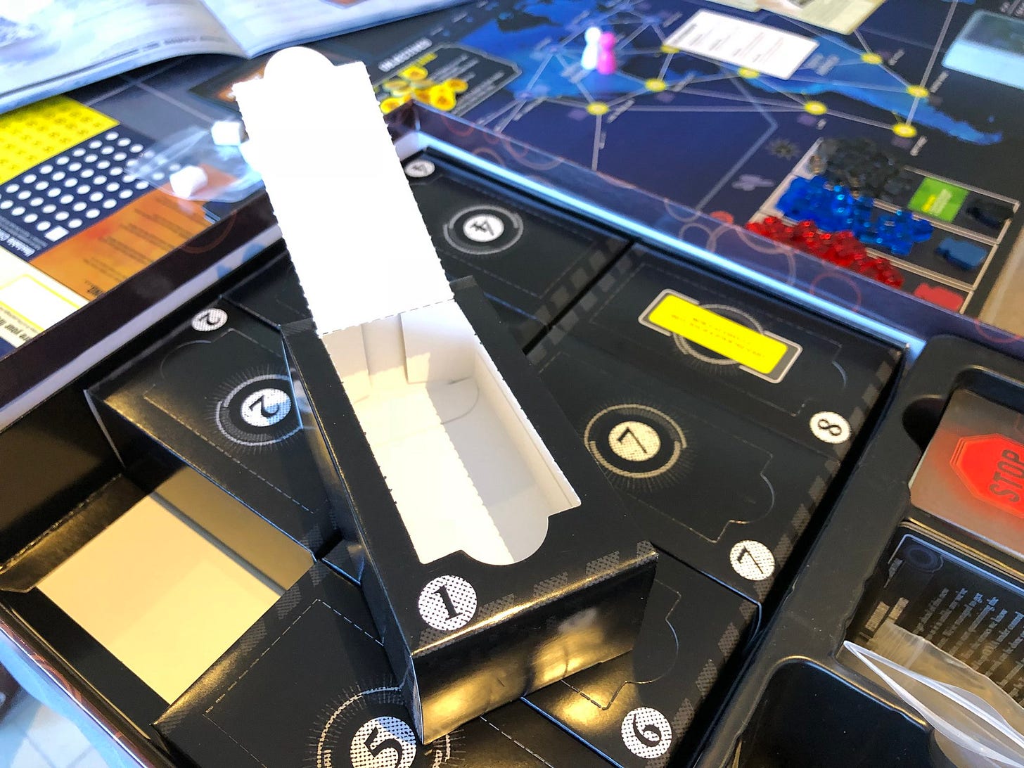 An open cardboard box labled "1" on top of the box of Pandemic Legacy filled with other numbered boxes.