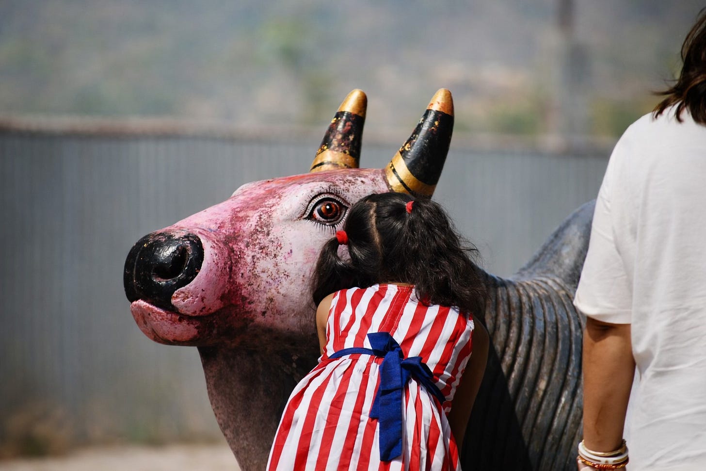 A girl is leaned forward whispering n the ear of a statute of a bull. A girl is leaned forward whispering n the ear of a statute of a bull.