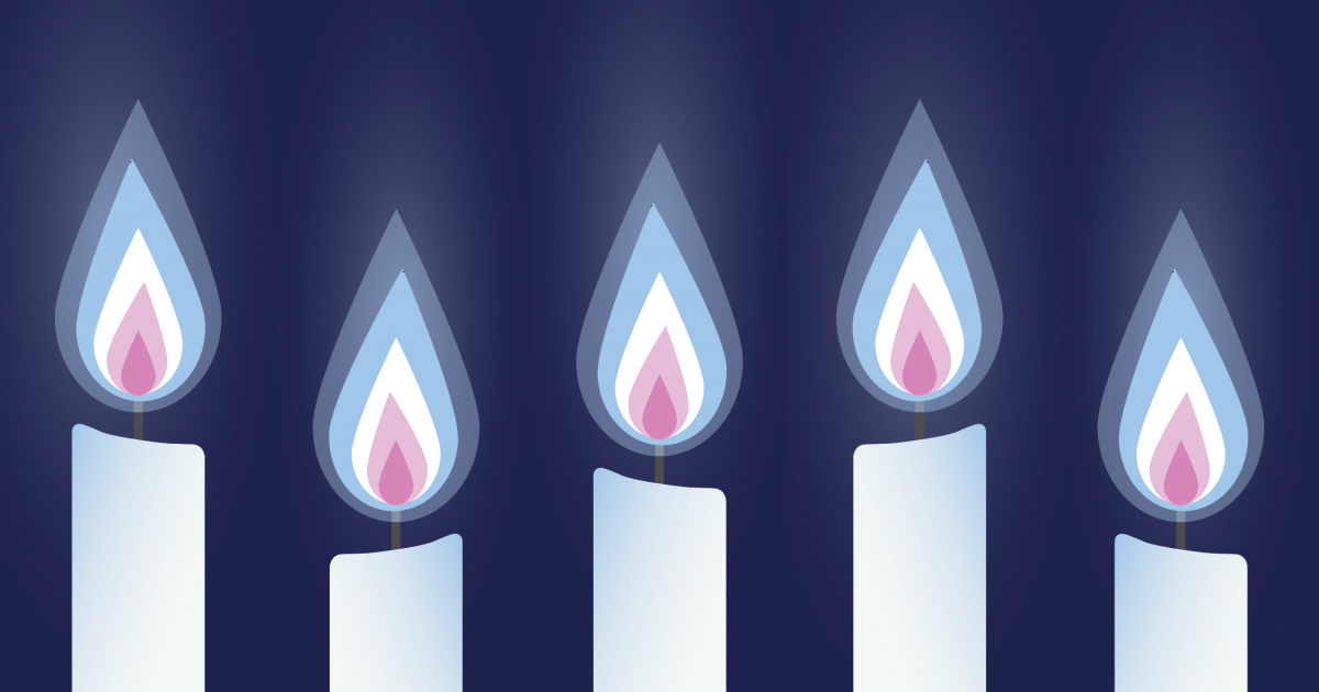 Row of glowing memorial candles with flames in the colors of the transgender pride flag—blue, pink, and white—set against a dark background, symbolizing remembrance, solidarity, and honor for Transgender Day of Remembrance.