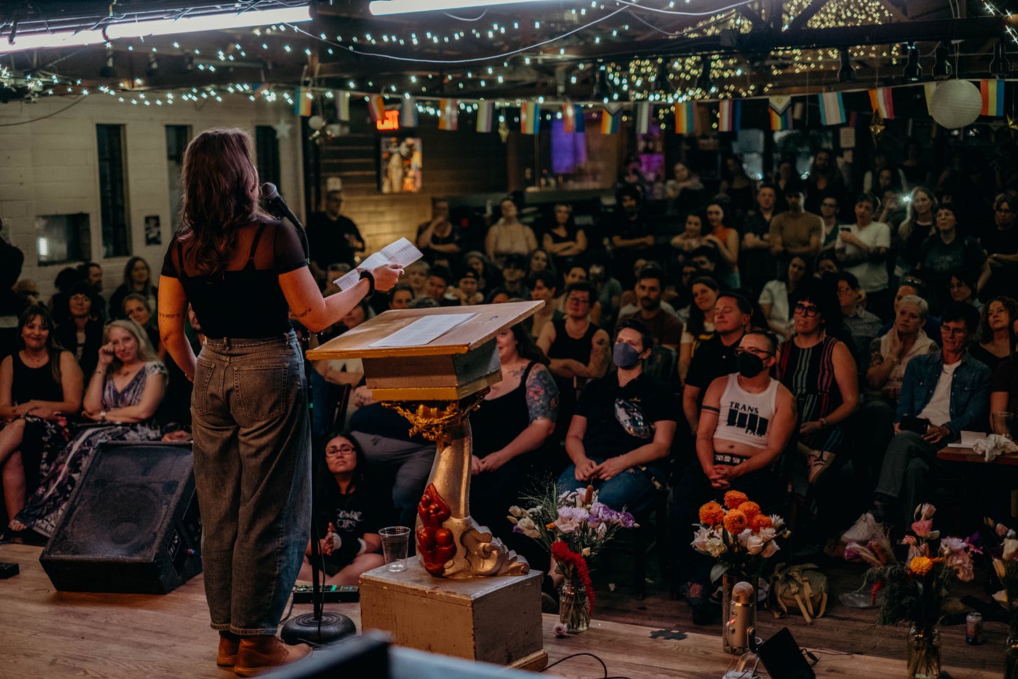 In a light-strung room, Meg reads one of Andrea's poems to an audience of hundreds in Denver, many of whom are crying.
