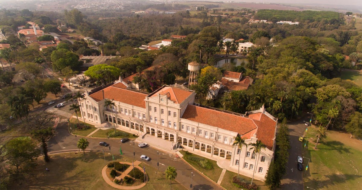 Visão aérea de construção antiga de dois andares no meio de uma área cheia de árvores e na frente um gramado