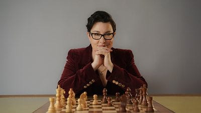Sue Perkins in a burgundy velvet blazer sat in front of a chess board with her game face on