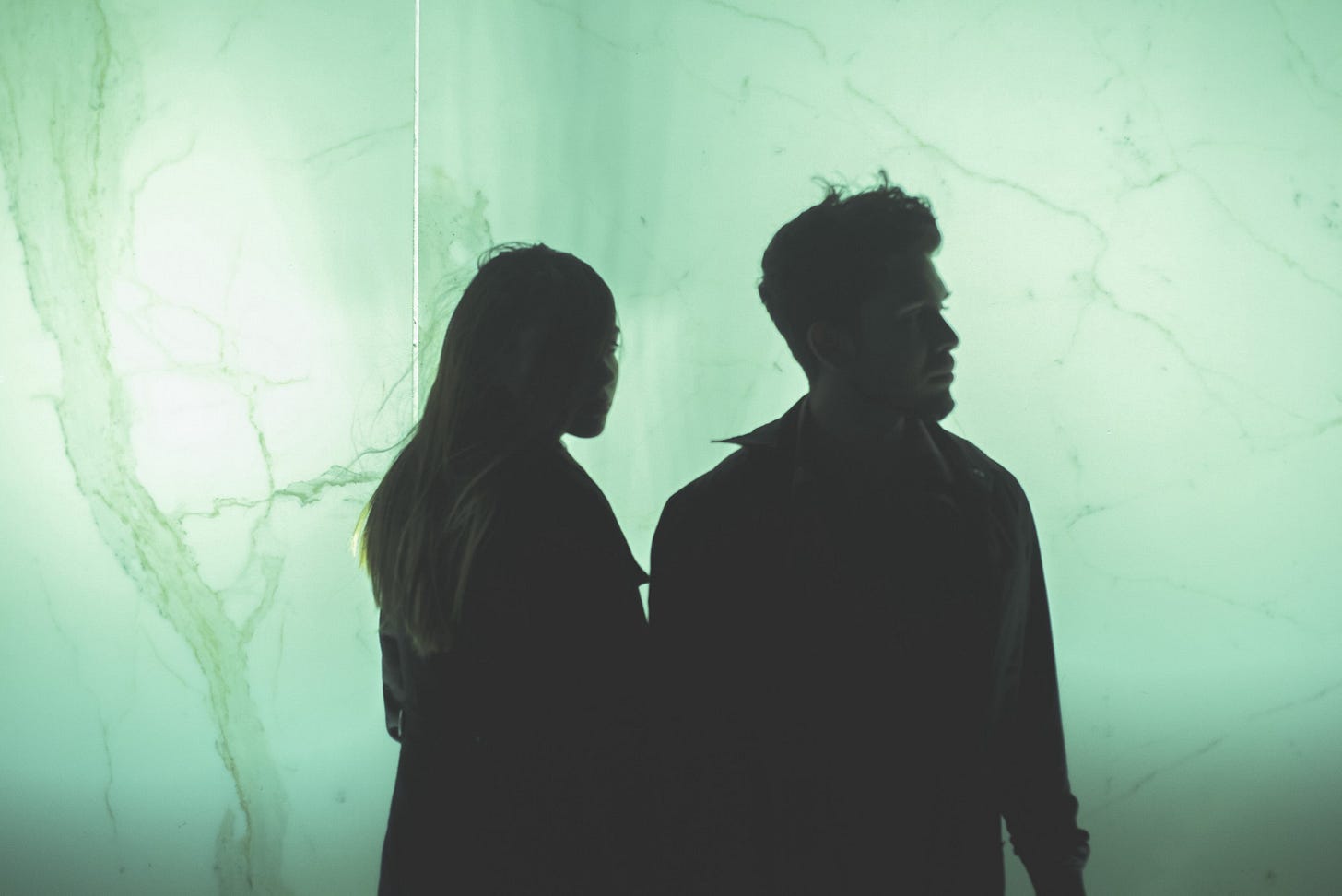 The silhouette of a couple walks down a green marble hallway.