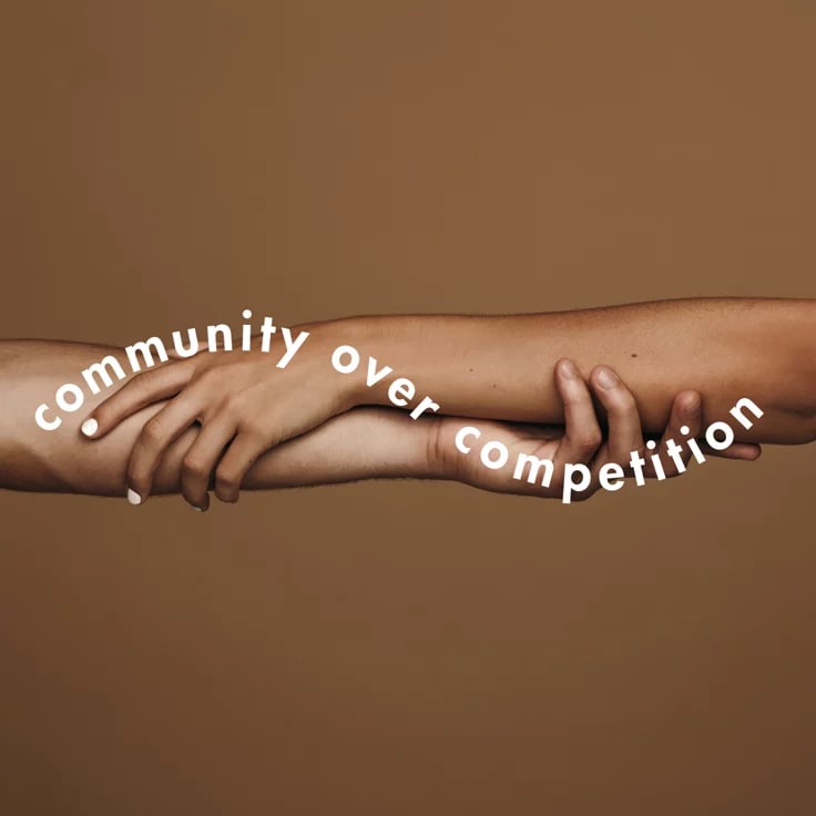 This may contain: two hands holding each other with the words community over competition written on their palms, in front of a brown background