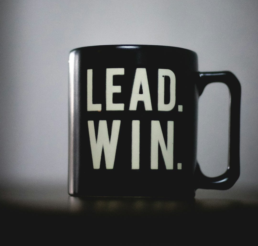 a black coffee mug with the words lead win printed on it