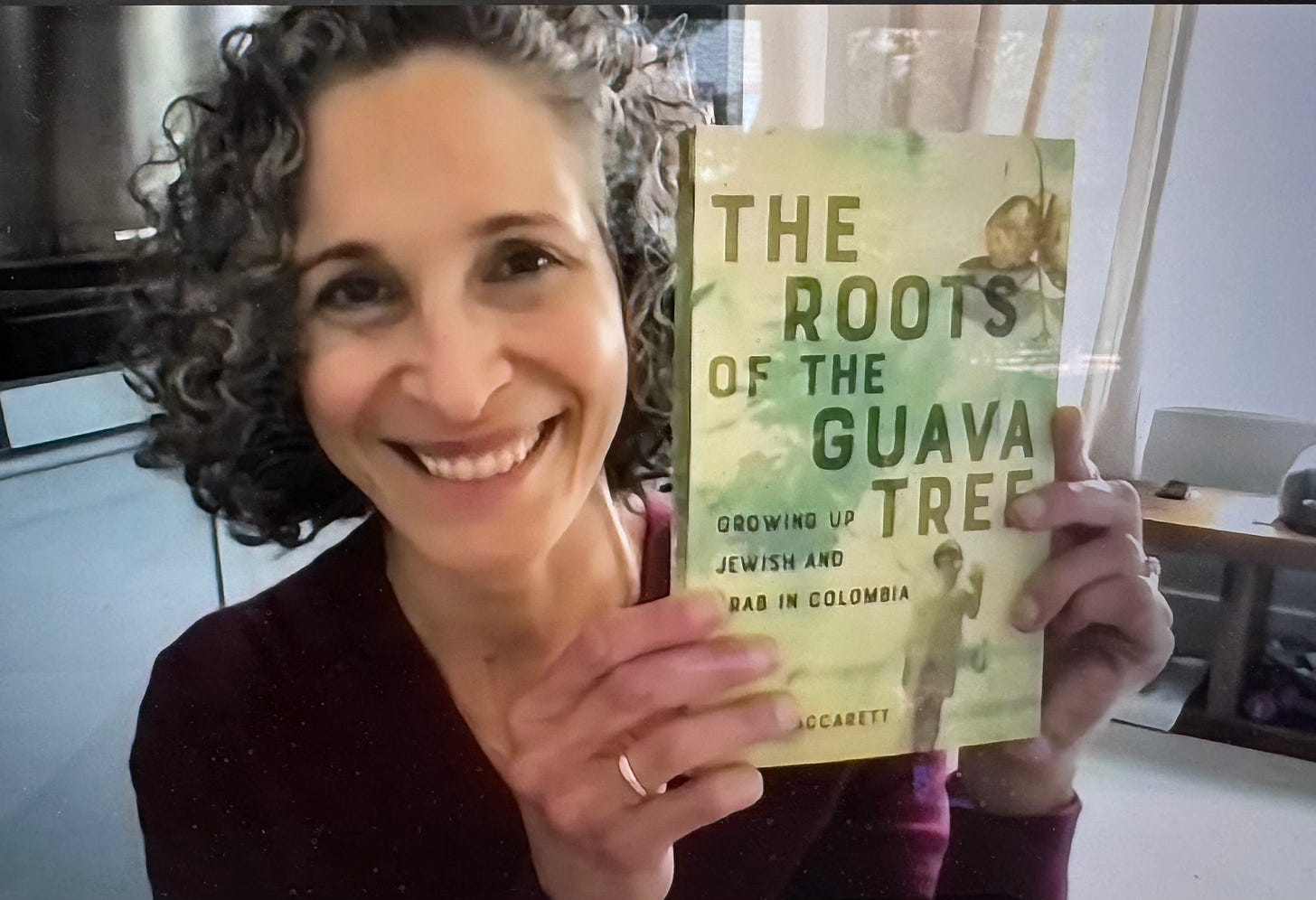 Close up of woman smiling holding up book. She has a ring on her wedding finger.