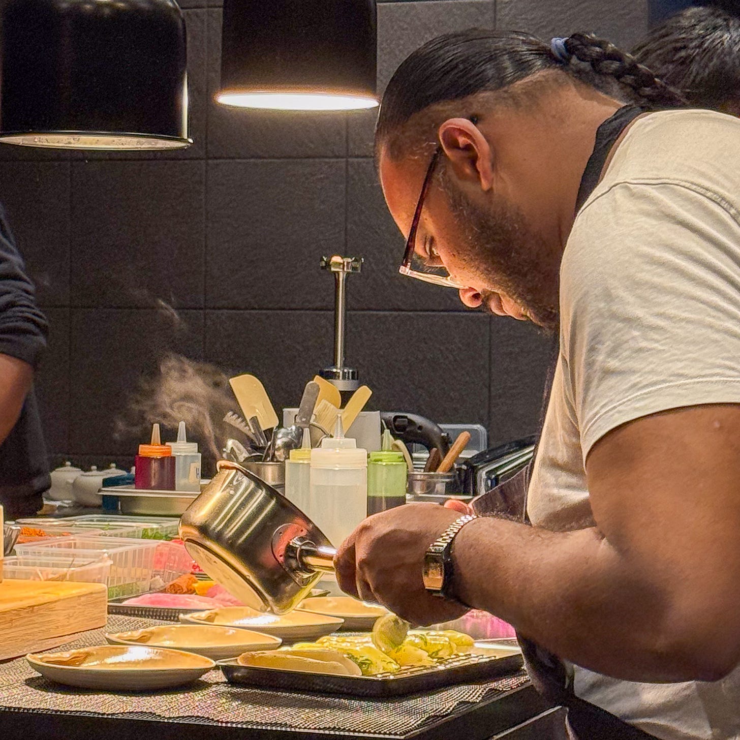Chef Manogeran Shasitharan plating dishes at the open kitchen pass at Mantra restaurant with squeeze bottles and cooking equipment visible