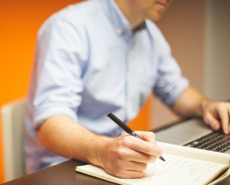 man in white business shirt writing on paper at a desk. man in white business shirt writing on paper at a desk.