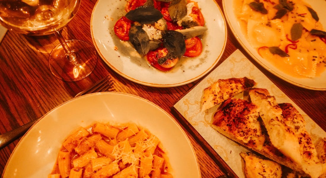 A wooden table with rigatoni, salad, ravioli, and bread on it A wooden table with rigatoni, salad, ravioli, and bread on it