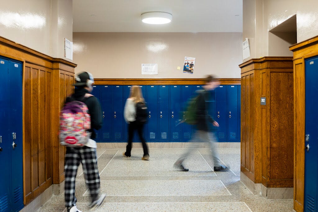 Students walk in a school hallway with blue lockers.