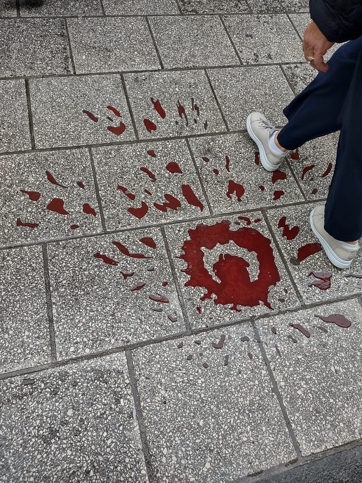 Pictures of a red splotch mark on the ground. It is the indent of a bomb indentation.