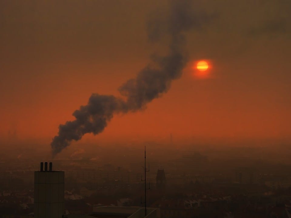 Smoke billows from a chimney against a hazy sunset.
