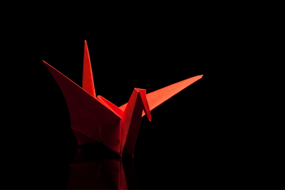 red paper crane on a black background and reflective surface