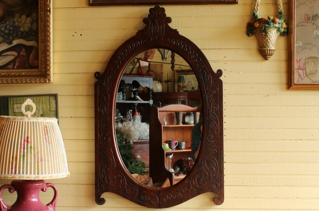 a mirror sitting on top of a wooden table next to a lamp