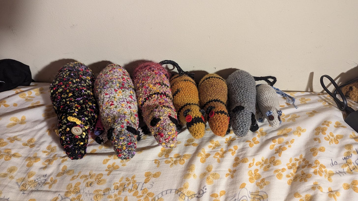 seven colorful crocheted rats. some of them have button eyes and all of them have two tails