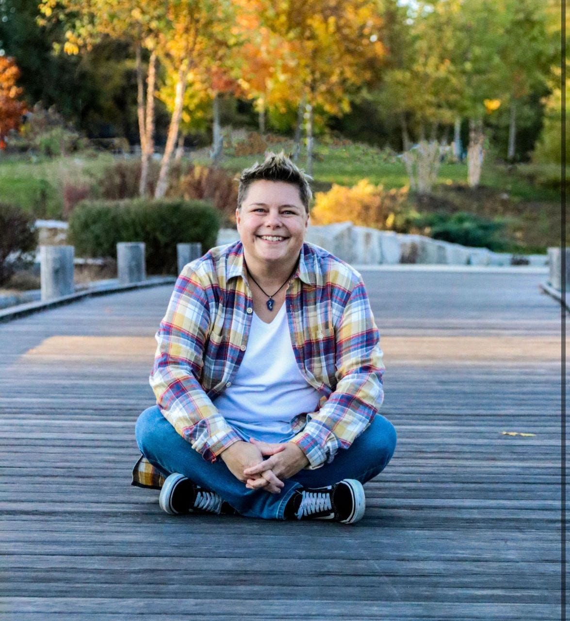 A smiling Chris Davis sits on a wooden walking bridge with autumn foliage in the background.