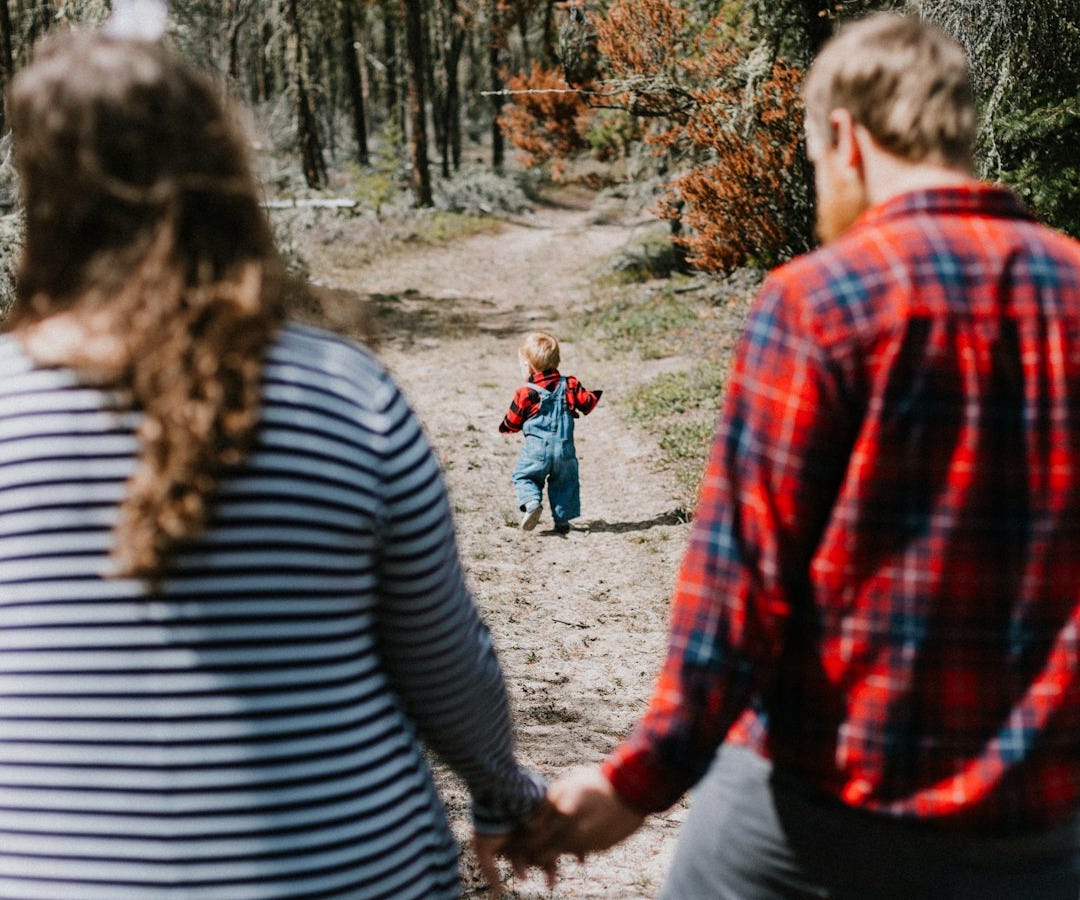 a man and a woman holding hands while walking down a dirt road