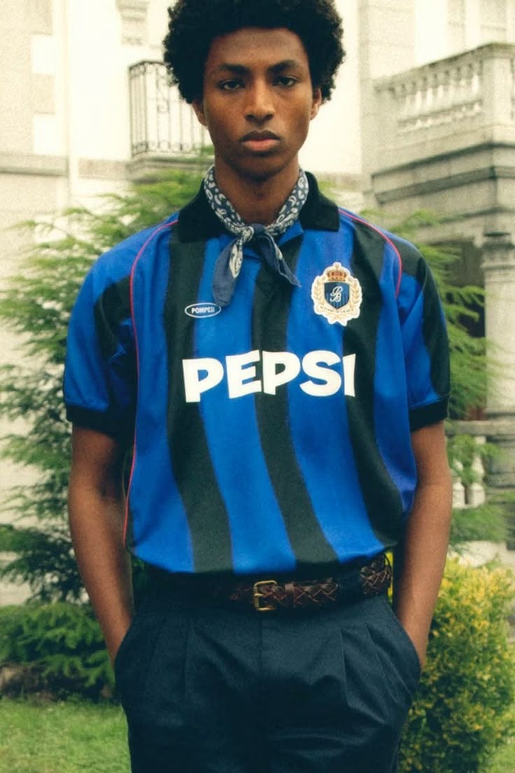 This may contain: a young man standing in front of a building wearing a blue and black striped shirt