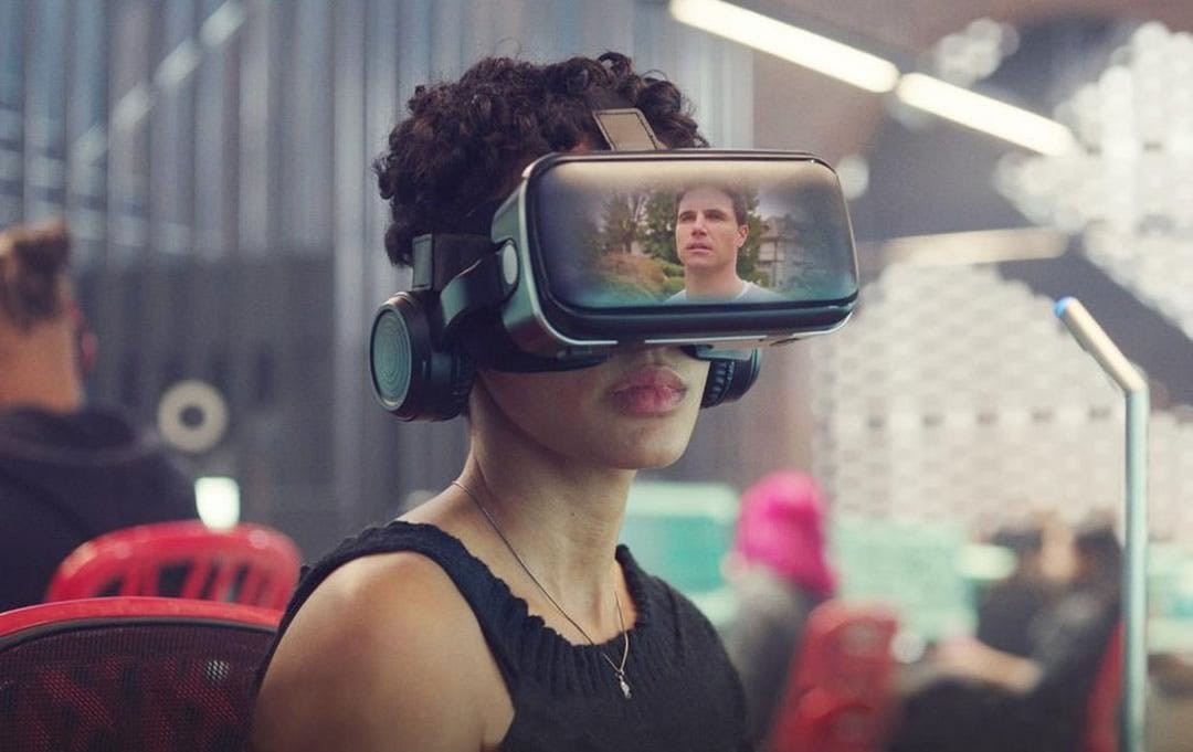 Imagem de uma mulher num escritório usando um dispositivo VR para observar a imagem de um homem, mostrado na tela dos óculos