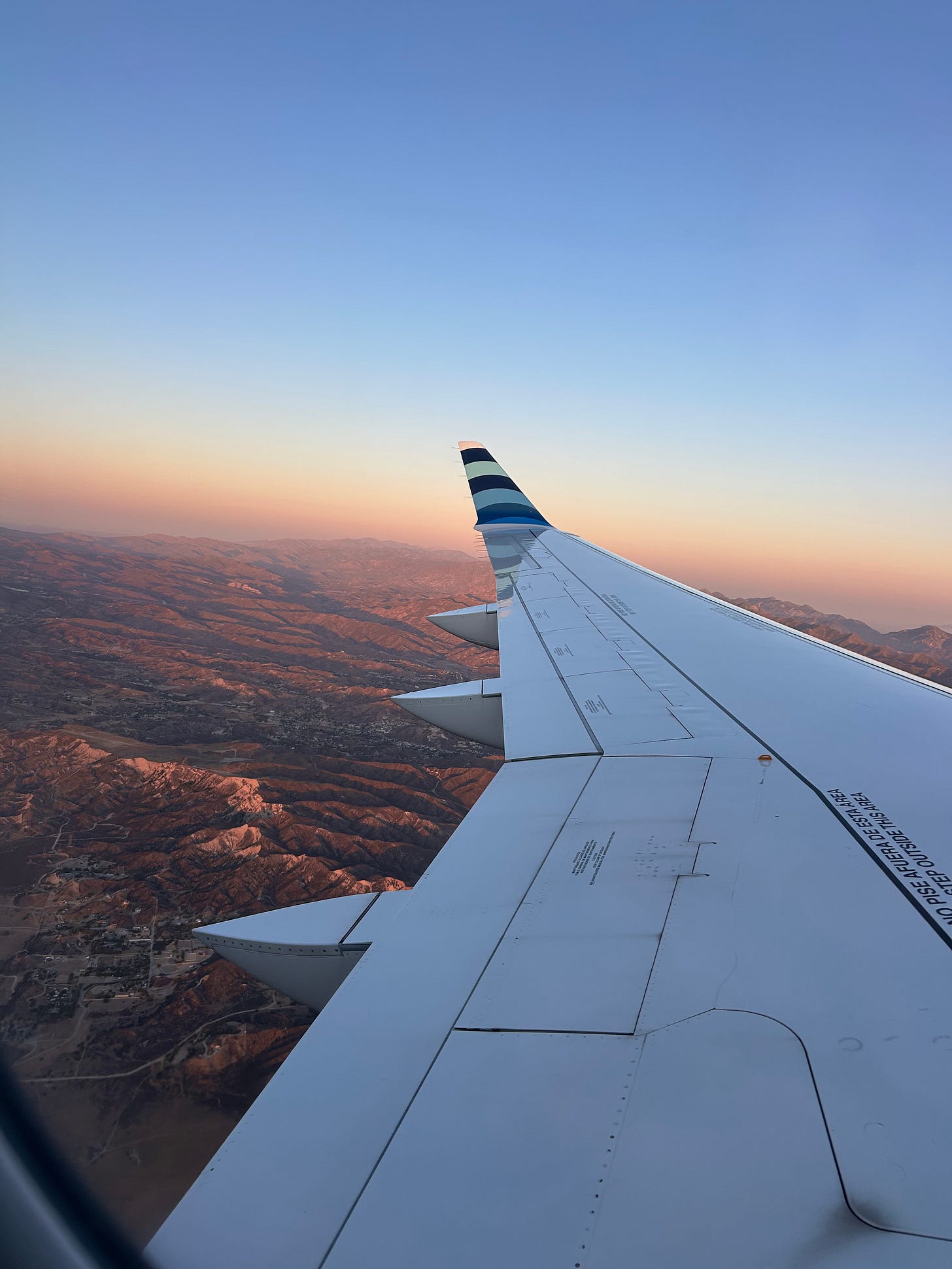 the wing of a plane over sunset-lit burbank mountains