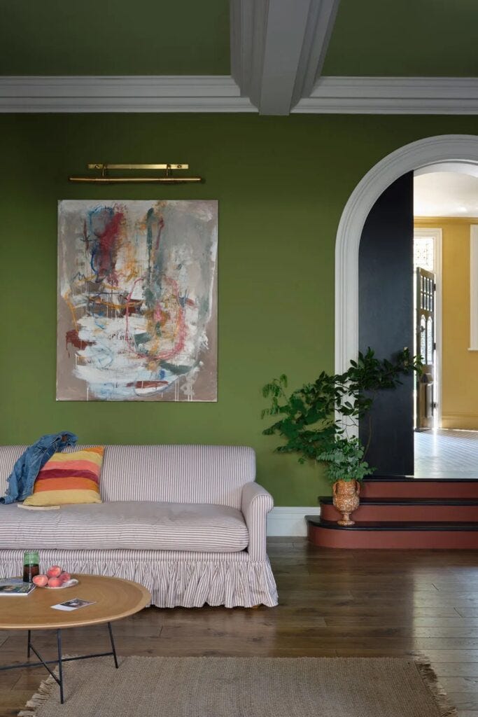 A living room featuring a deep green wall painted in new Farrow & Ball colour Sap Green, complemented by a striped skirted sofa, abstract artwork, and a cozy, eclectic mix of textures and colors. A living room featuring a deep green wall painted in new Farrow & Ball colour Sap Green, complemented by a striped skirted sofa, abstract artwork, and a cozy, eclectic mix of textures and colors.