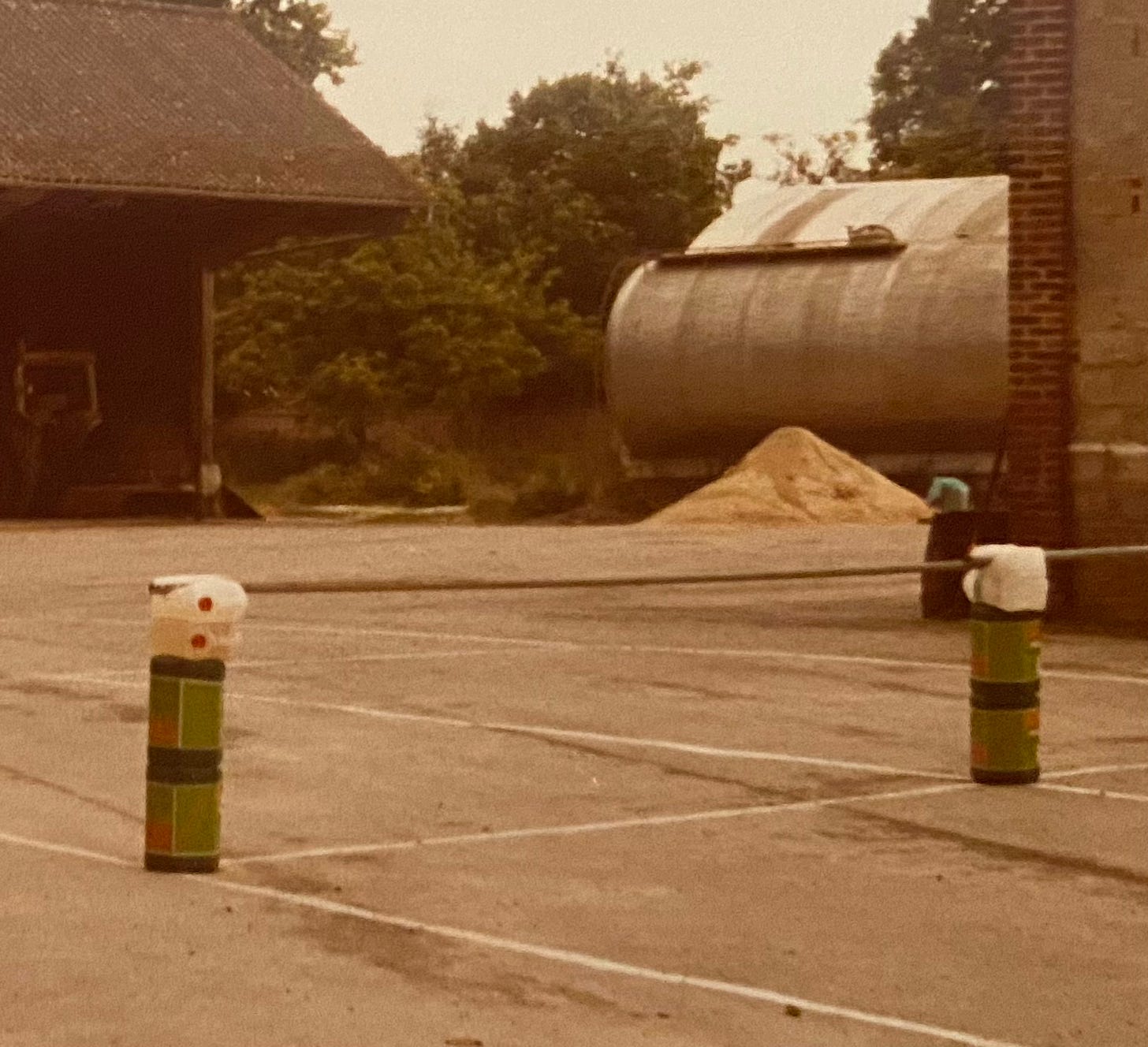A tennis court in a farmyard courtyard with drums, plastic bottles and a steel rod for a net.