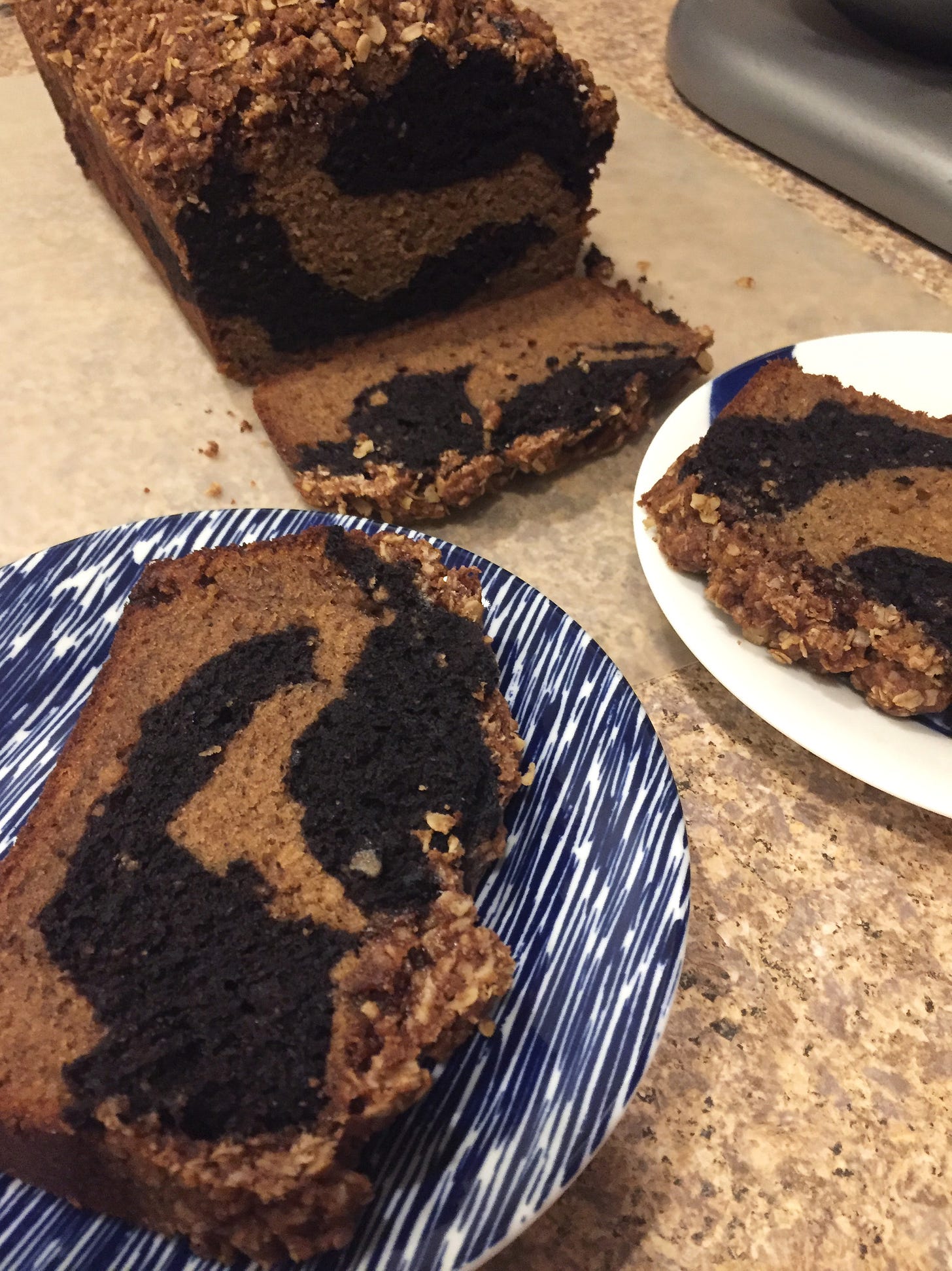 On a thin cutting board, a marbled loaf of banana bread with the cut side facing the camera. Two slices sit in the foreground on small blue and white plates.