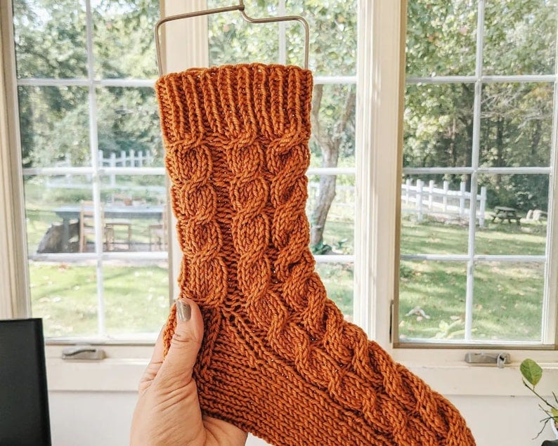 May include: A knitted sock in a brown color with a cable knit pattern.