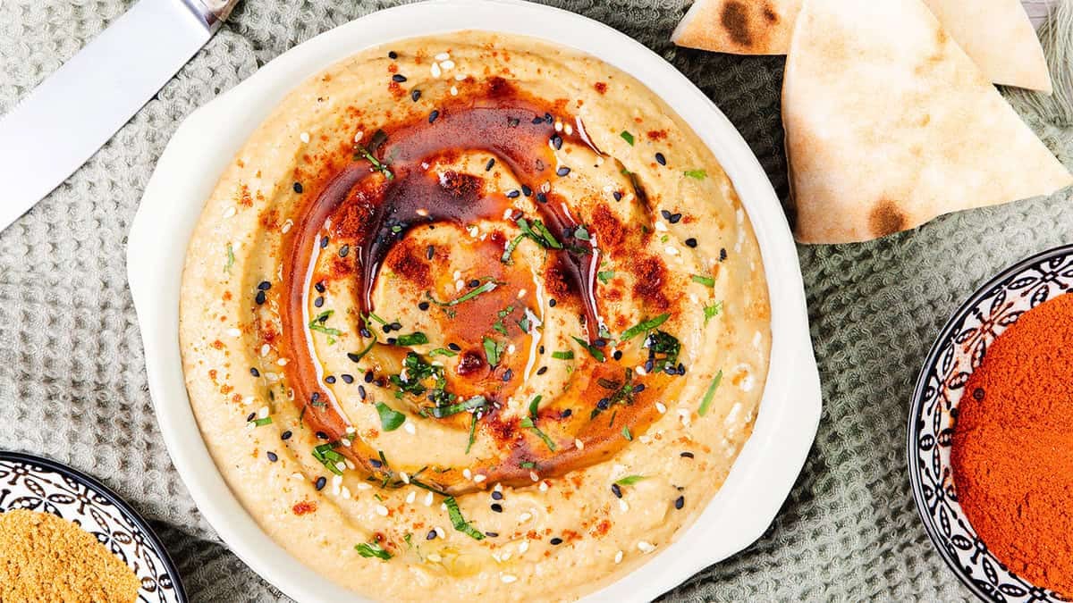 Creamy baba ganoush topped with olive oil, paprika, sesame seeds, and fresh herbs, served with warm pita bread.