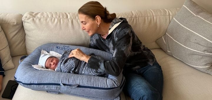 A woman seated on a couch, looking down at a newborn baby