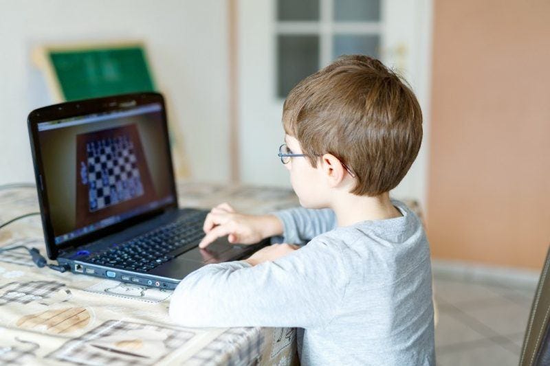 young boy playing online chess on laptop young boy playing online chess on laptop
