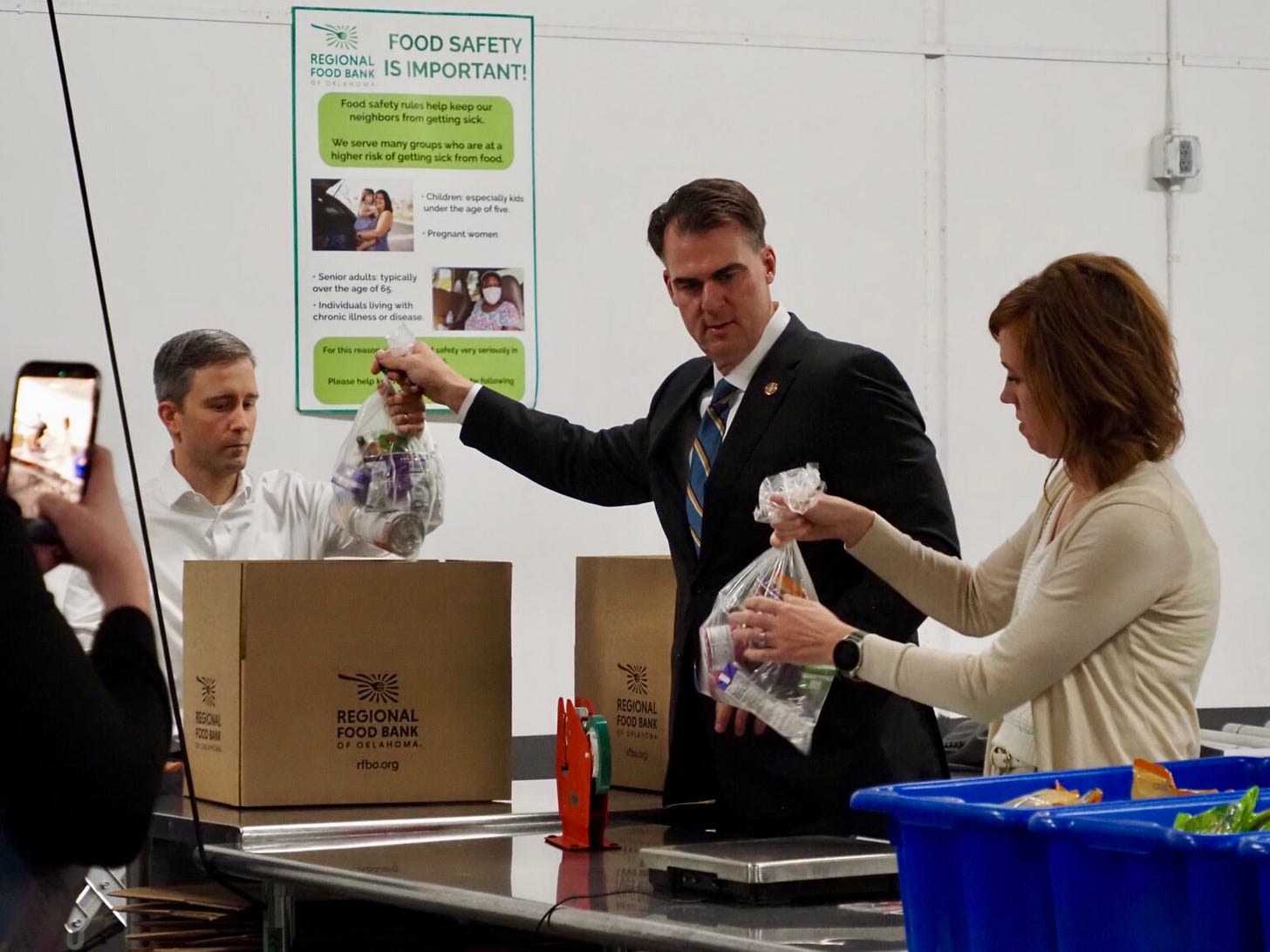  Gov. Kevin Stitt, center, helps to pack boxes at the Regional Food Bank of Oklahoma on Oct. 29, 2025, with his chief of staff Donelle Harder, right, and Jeffery Cartmell, director of the Oklahoma Department of Human Services, left. (Photo by Emma Murphy/Oklahoma Voice)