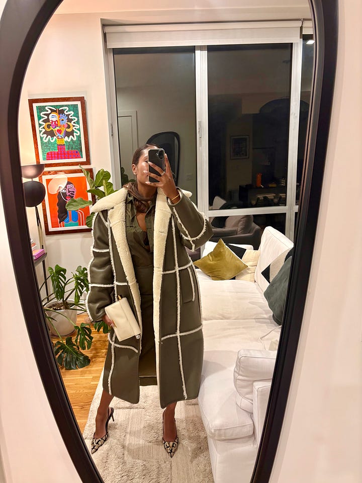 Two, full body mirror selfie photos side by side showing Black woman posed in a beautiful olive green monochrome outfit including an oversized, sherpa lined long leather coat and two-piece sheer collard button-up top and maxi skirt.