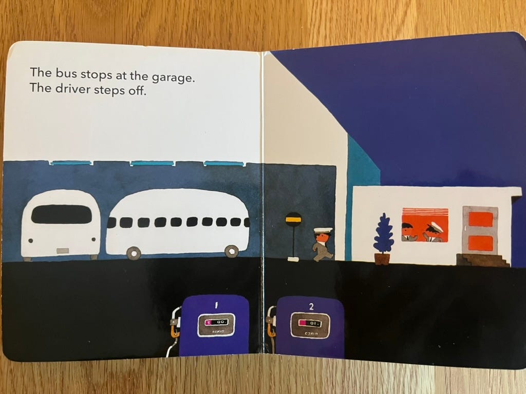 A picture book page, with the text "The bus stops at the garage. The driver steps off." The picture shows a bus garage with 2 buses parked inside, and a bus driver walking toward a smaller building where 2 other drivers are inside and talking to each other. A picture book page, with the text "The bus stops at the garage. The driver steps off." The picture shows a bus garage with 2 buses parked inside, and a bus driver walking toward a smaller building where 2 other drivers are inside and talking to each other.