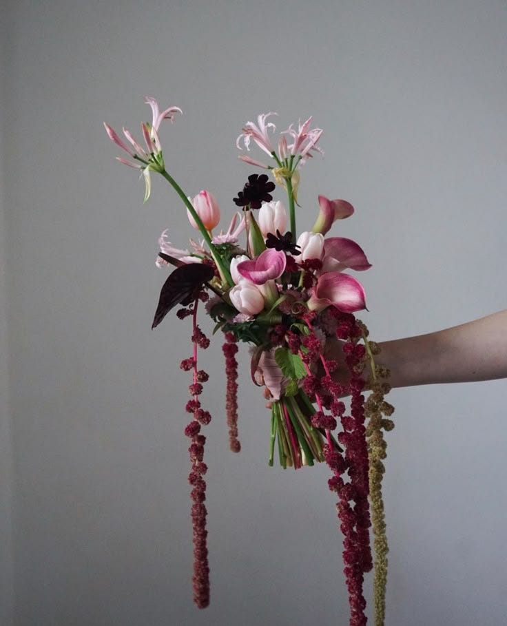 This may contain: a person holding a bouquet of flowers in their hand with beads hanging from the stems