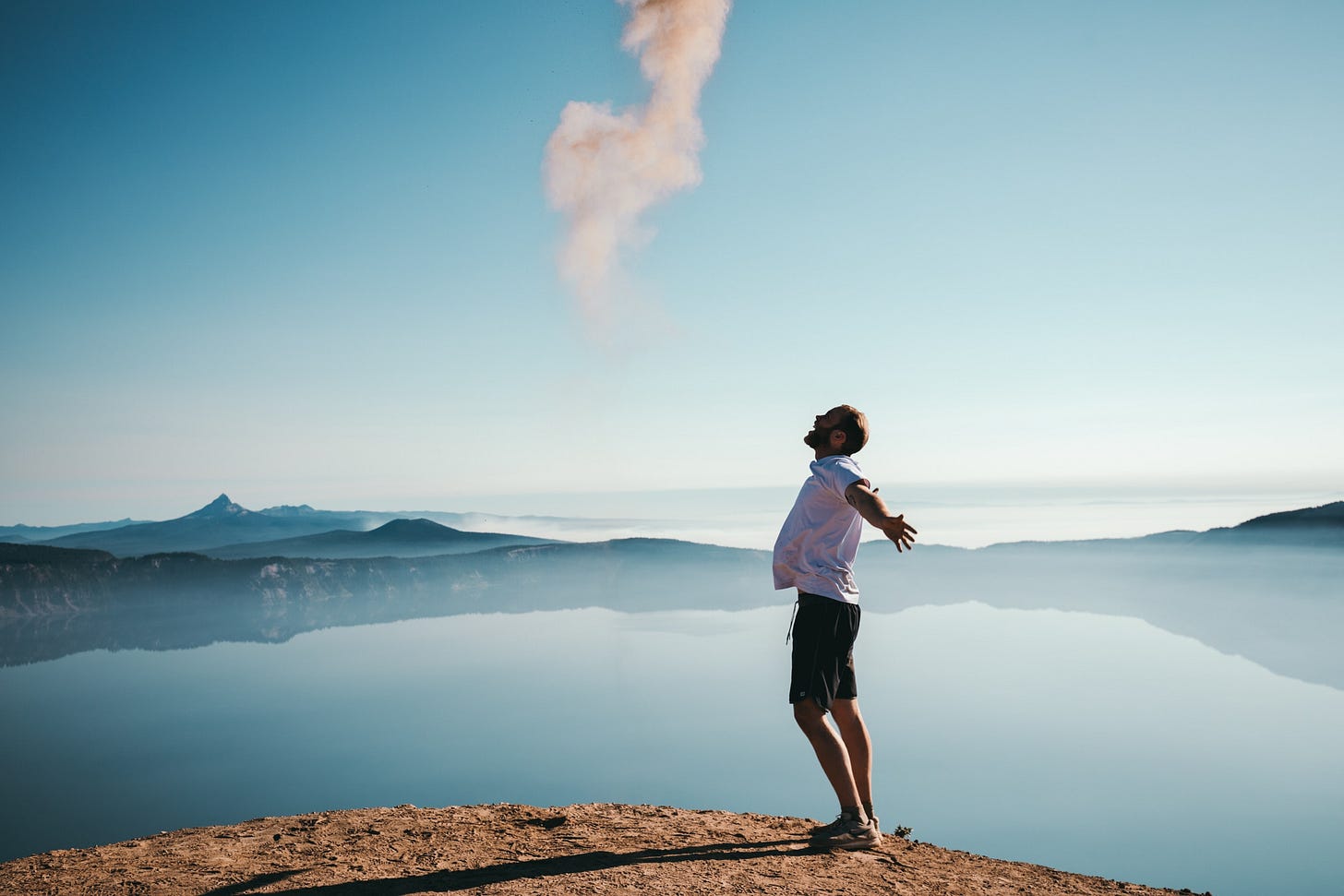 A white man stands in front of a mountain lake and jumps with his arms kind of behind him. He looks really happy but in a very corporate, posed kind of way A white man stands in front of a mountain lake and jumps with his arms kind of behind him. He looks really happy but in a very corporate, posed kind of way