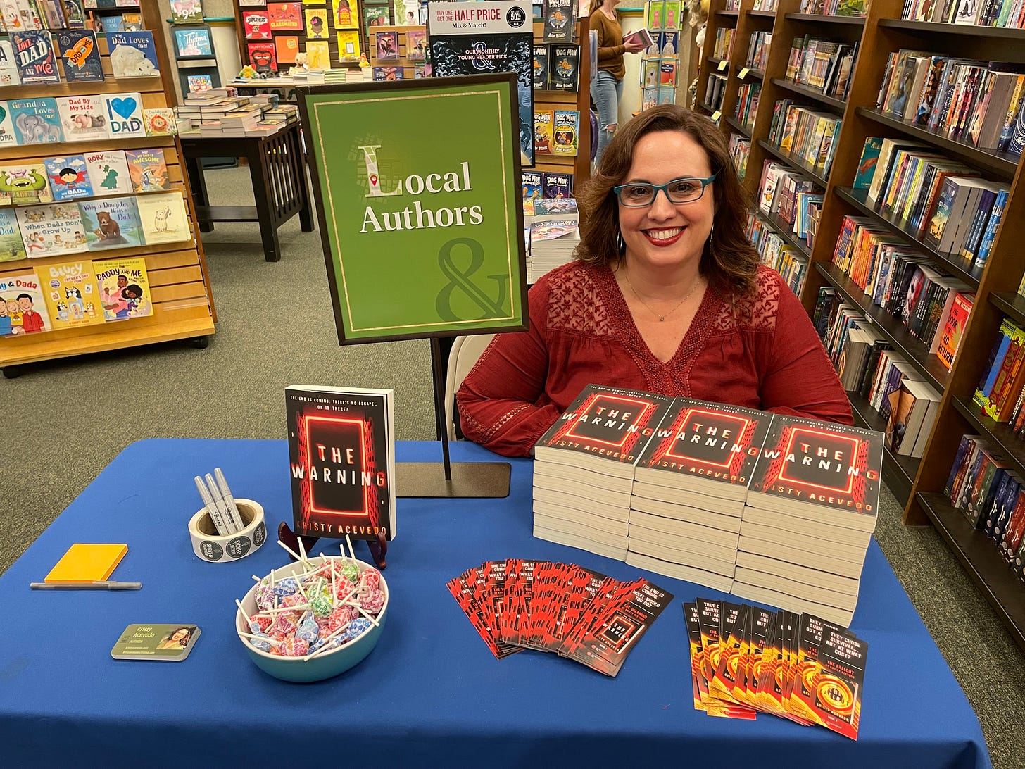 Me sitting at a small table with THE WARNING books and a sign that reads Local Author at a Barnes and Noble