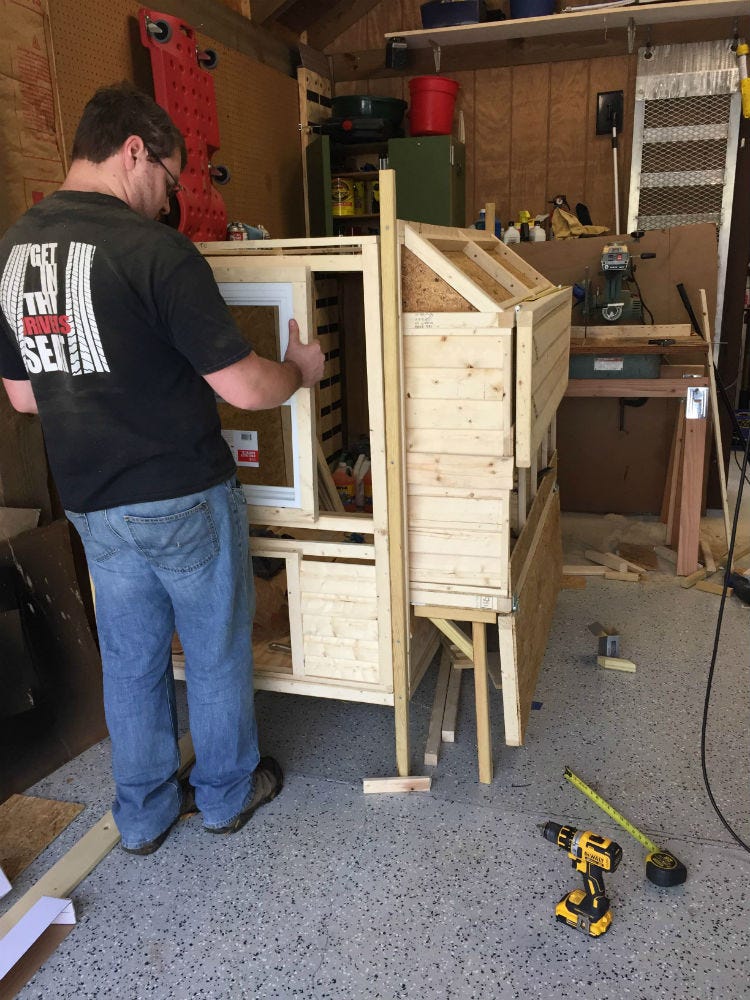 person sizing a small window on a chicken coop under construction