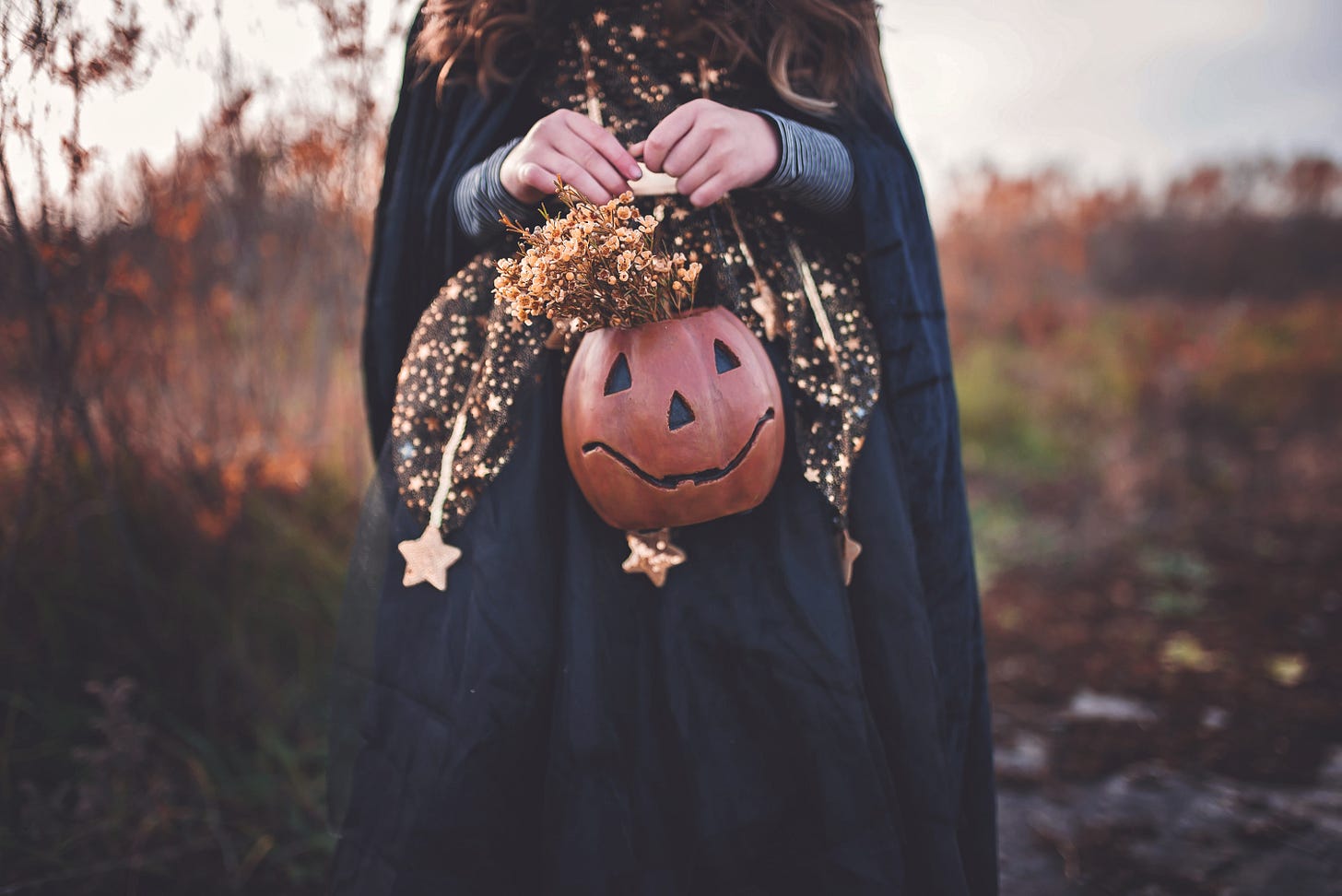 Girl in Black holding jack o'lantern with flowers.