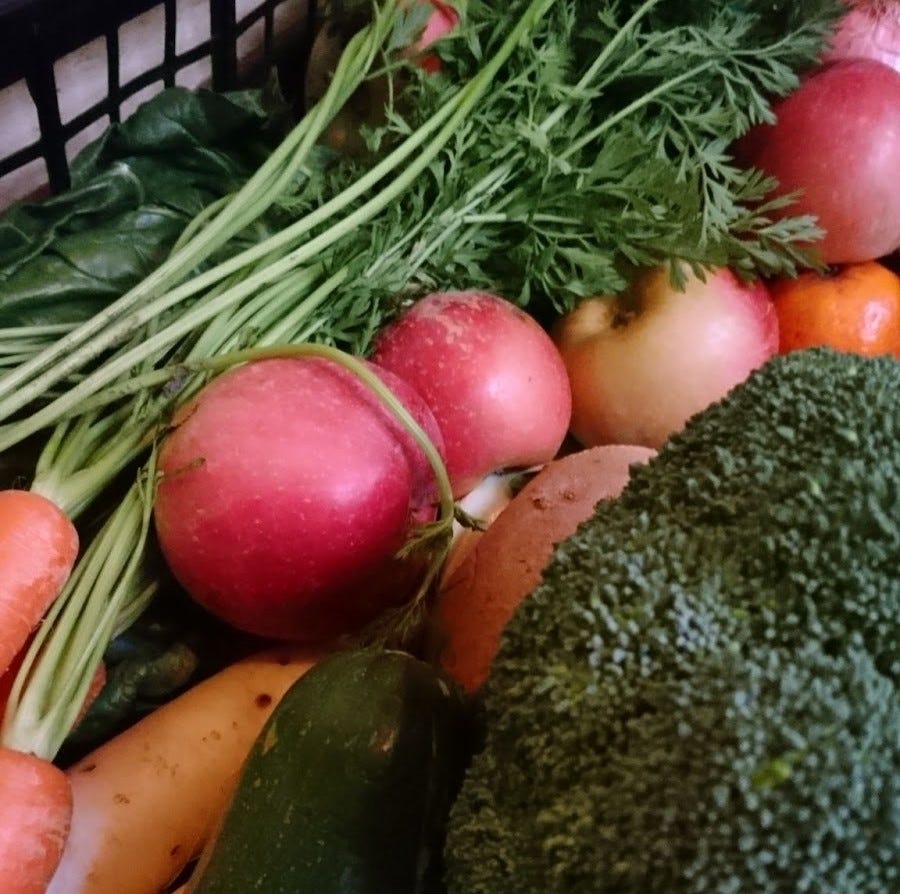 Photo of a black basket of apples, spinach, broccoli, kale and other vegetables
