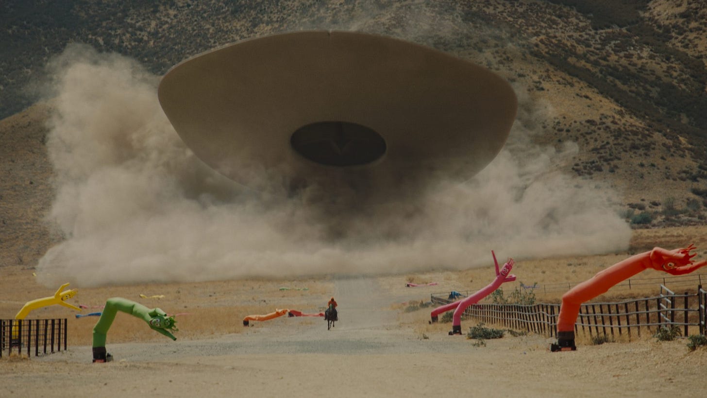 An image of O.J. riding his horse away from the alien Jean Jacket while inflatable tube men collapse on the ground.