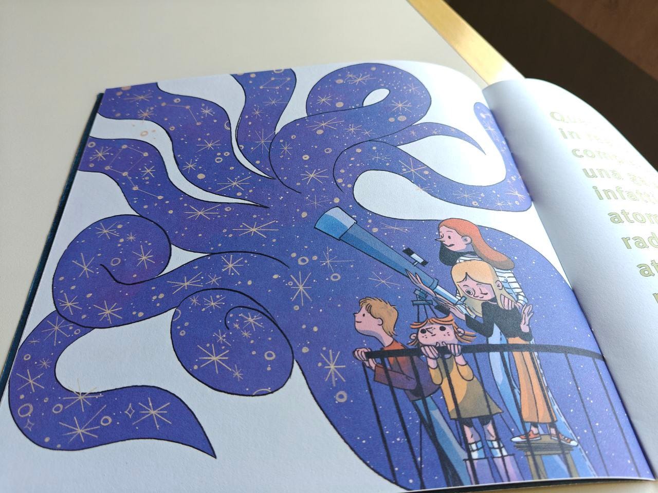Pagina illustrata della Scatolina SPAZIO edita da effequ, appoggiata su un tavolo di legno color bianco sporco, con un pezzetto di muro in ombra nell'angolo in alto a destra. Su un balcone in basso a destra ci sono due bambini, una bambina e una ragazza dalla pelle chiara che sono intente a guardare il cielo attraverso un telescopio. Il cielo è di colore azzurro-viola e pieno di stelle, ma prende la forma di una specie di morbida piovra, con i tentacoli che si stagliano su uno sfondo bianco.