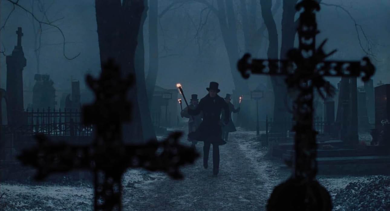 A still from the film. Three men bearing torches dash into a dimly lit cemetery.