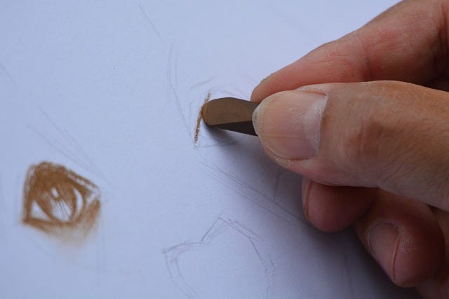 Mano che disegna su un foglio bianco con un pastello marrone, concentrandosi sui dettagli di un occhio. Mano che disegna su un foglio bianco con un pastello marrone, concentrandosi sui dettagli di un occhio.