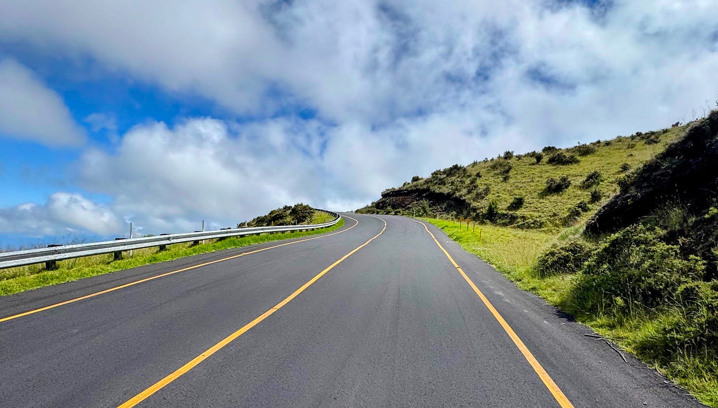 A two-lane road on Haleakala bending out of sight around a rising corner.