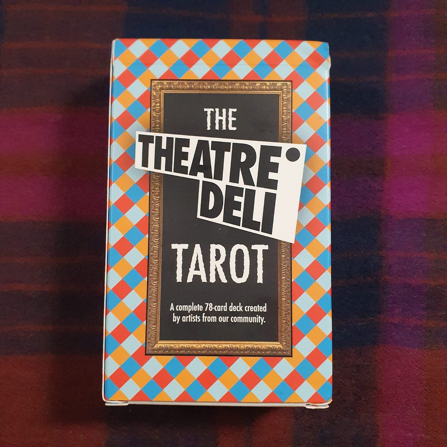 Box of The Theatre Deli Tarot, a complete 78-card tarot deck created by artists from the Theatre Deli community, photographed on a dark patterned surface. Image from the Amy Twigg Tarot DMs interview featuring the deck used for her tarot reading. Box of The Theatre Deli Tarot, a complete 78-card tarot deck created by artists from the Theatre Deli community, photographed on a dark patterned surface. Image from the Amy Twigg Tarot DMs interview featuring the deck used for her tarot reading.