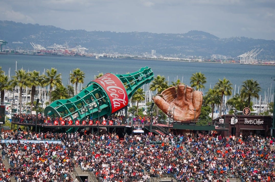 Giant coca-cola bottle and baseball glove dominate a stadium crowd.