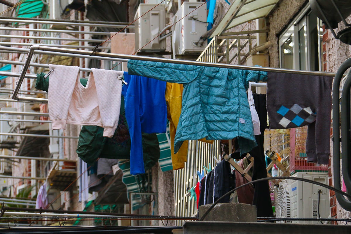 Teal, yellow, and cobalt clothes sway from shiny aluminum poles outside an apartment. A close-up burst of visual warmth on a cloudy day.