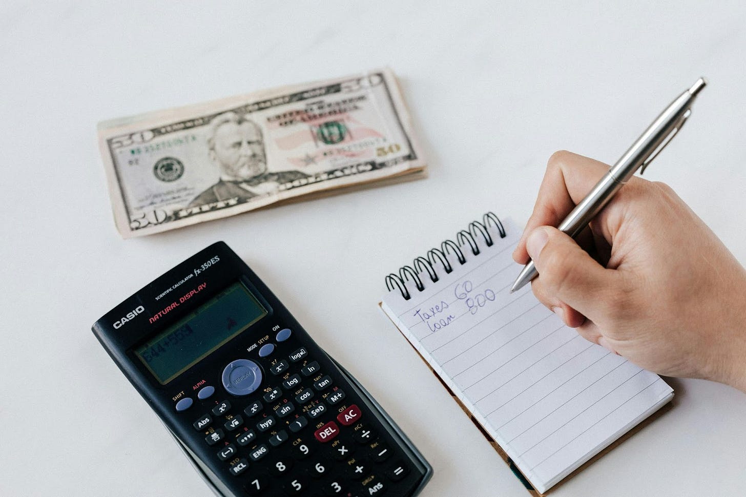 Hand writing on a notepad with calculator and dollar bills