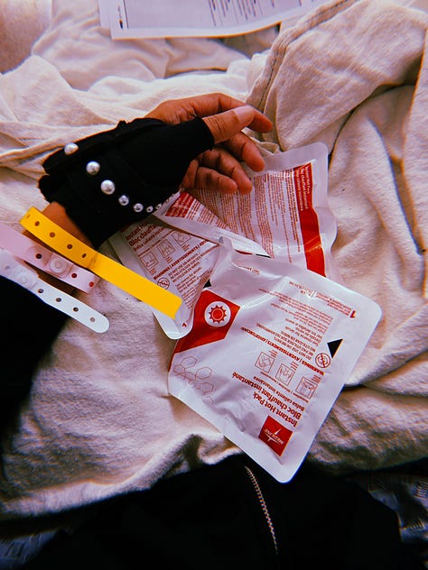 Images for Dr. Cadet in the ER from her braced left thumb adorned with pearls resting on heating packs. Her wrist with a yellow falls risk band, white medical ID band, red allergy band. Blue sheets, white pillow and cream heated blankets on a gurney and covering her like a burrito as she wears a floral mask in her ER room.